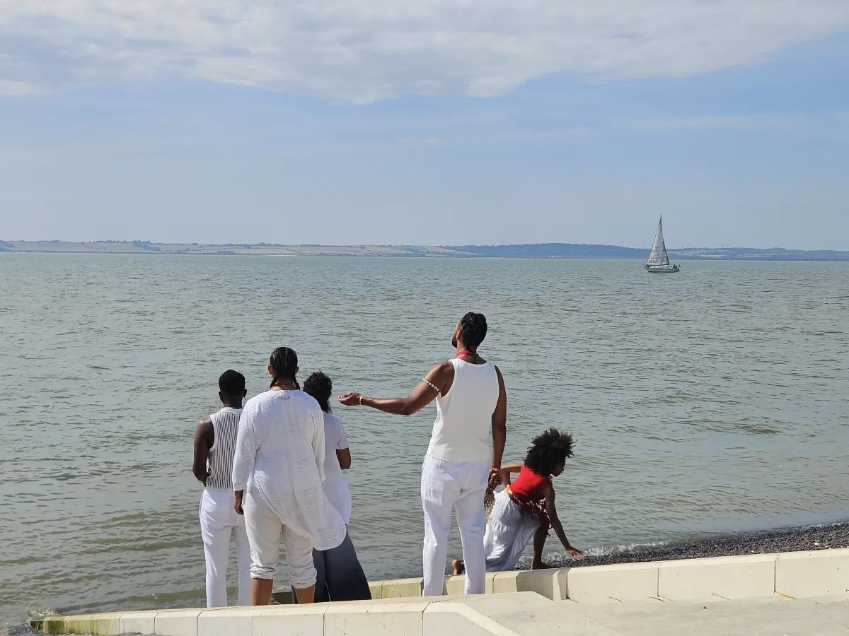 Choir singing in front of the Thames Estuary with a boat sailing in the distance